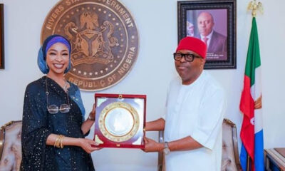 Two Nigerian officials exchange a framed award plaque in a government office, with the state seal on the wall behind them.