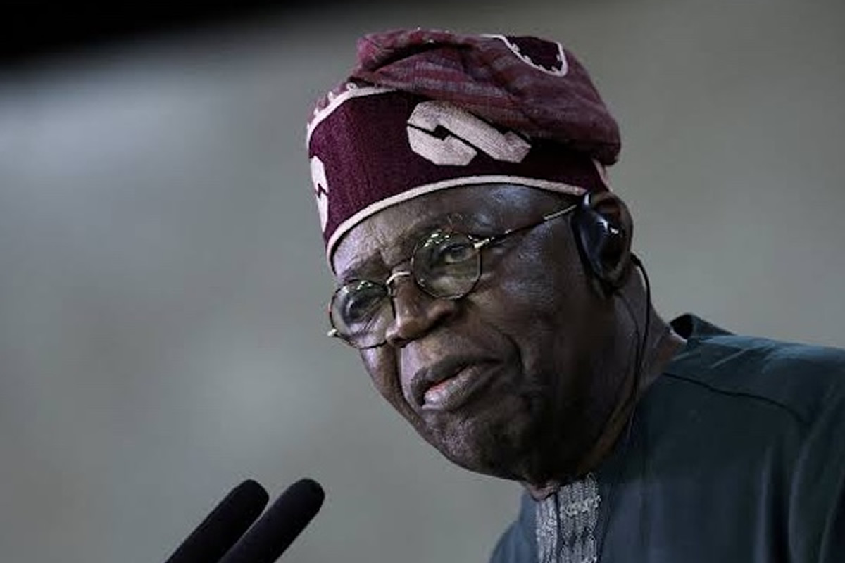 Older man wearing a maroon headwrap and round glasses speaks into two microphones.