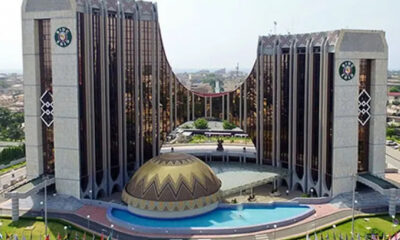 Aerial view of a U-shaped glass building with a gold-domed pavilion in front and a curved pool nearby.