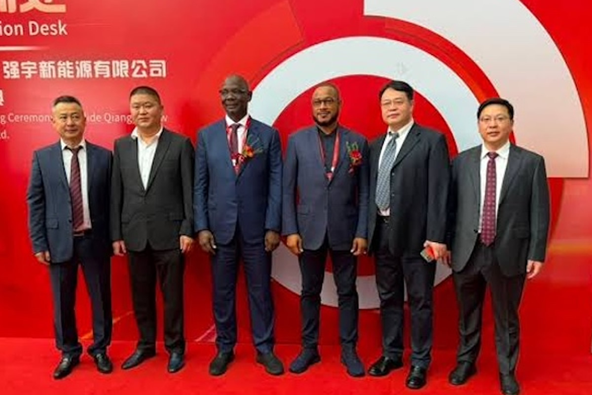 Six men in dark suits stand side by side on a red carpet at a corporate event, posing in front of a red backdrop with a white circular logo.