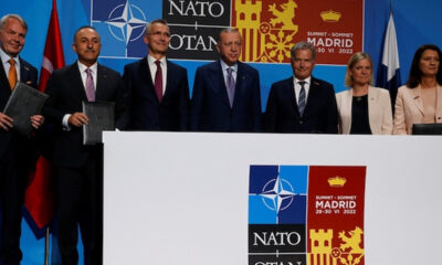 Group of officials in suits standing behind a podium at a NATO summit in Madrid 2022. Signs read NATO/OTAN and Madrid summit.