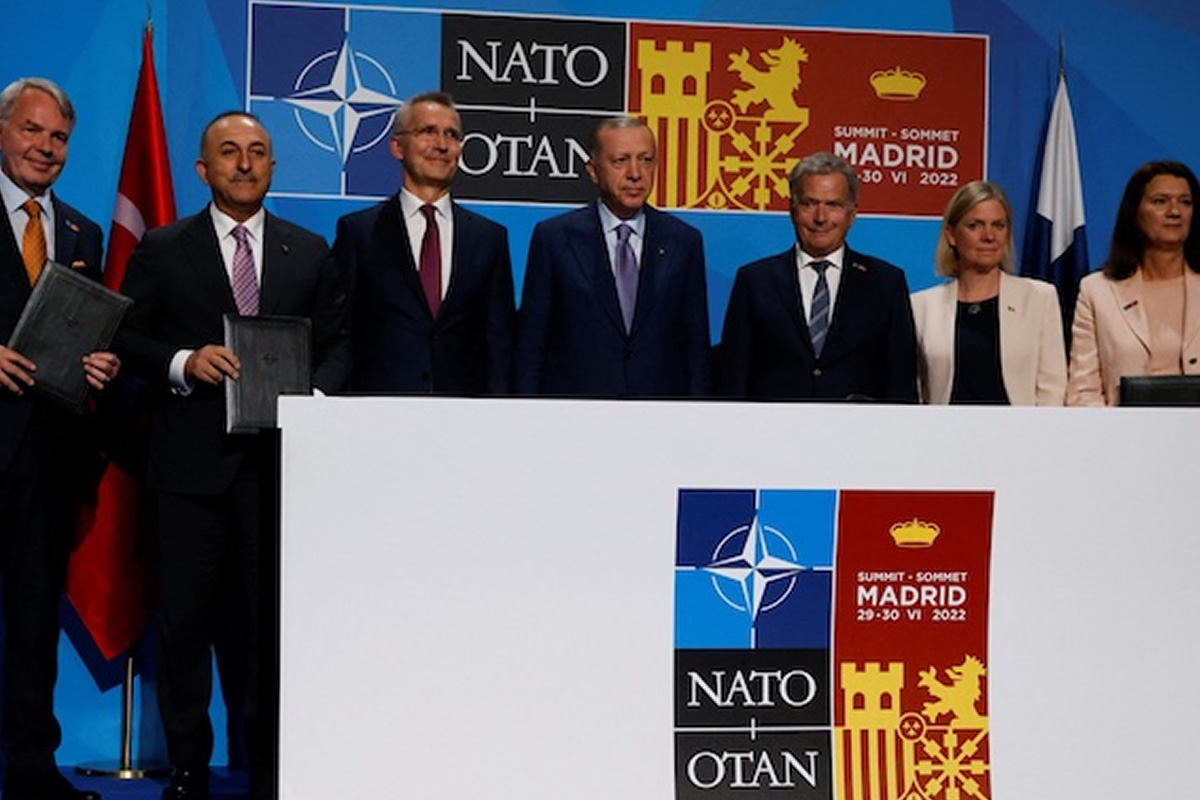 Group of officials in suits standing behind a podium at a NATO summit in Madrid 2022. Signs read NATO/OTAN and Madrid summit.