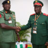 Two high-ranking African military officers in green uniforms shake hands at a formal meeting, with Nigeria and Guinea-Bissau flags visible on the table behind them.