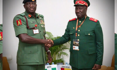 Two high-ranking African military officers in green uniforms shake hands at a formal meeting, with Nigeria and Guinea-Bissau flags visible on the table behind them.
