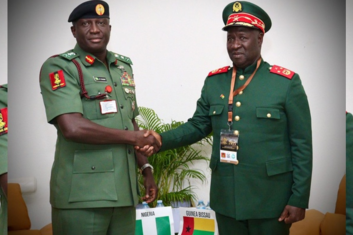 Two high-ranking African military officers in green uniforms shake hands at a formal meeting, with Nigeria and Guinea-Bissau flags visible on the table behind them.