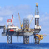 Offshore oil rig standing on pilings in the blue ocean under a clear sky.