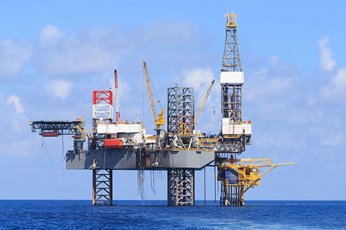 Offshore oil rig standing on pilings in the blue ocean under a clear sky.