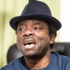 Man wearing a dark fedora hat and blue shirt, mouth open as if singing or speaking.