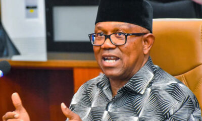 Man wearing glasses and a black cap speaks, gesturing with his hands at a formal meeting.