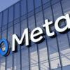 Meta logo with a blue infinity symbol and white letters on a glass office building facade against a blue sky