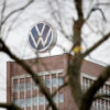 Volkswagen logo on a brick office building, framed by bare tree branches in the foreground.