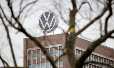 Volkswagen logo on a brick office building, framed by bare tree branches in the foreground.