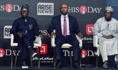 Three men sit on a stage in formal attire during a panel discussion, backdrop shows logos ARISE NEWS and THIS DAY.
