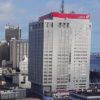 Tall white office building with a red UBA sign on top, overlooking a dense cityscape and harbor.