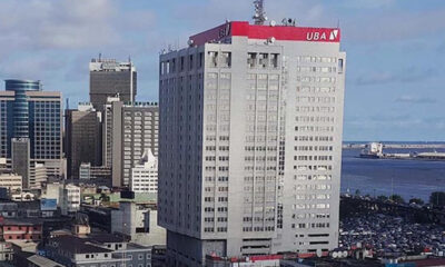 Tall white office building with a red UBA sign on top, overlooking a dense cityscape and harbor.
