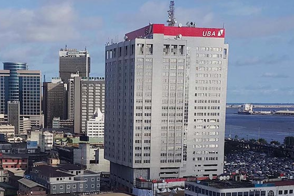 Tall white office building with a red UBA sign on top, overlooking a dense cityscape and harbor.