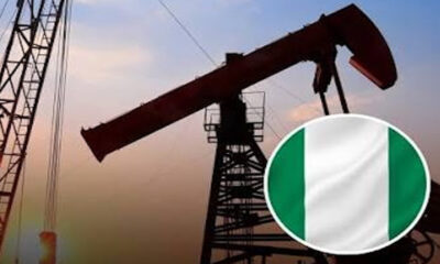 Oil pump jack silhouettes at sunset with a circular Nigerian flag badge in the foreground.