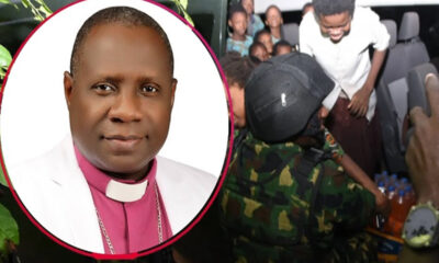 Portrait of a bishop in pink clerical attire and white robe, overlaid on a crowd as uniformed soldiers distribute bottled drinks in a bus or shelter scene.