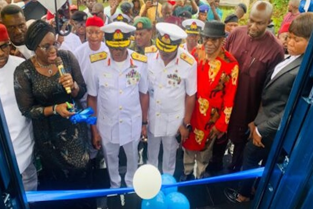 Group of officials at a ribbon-cutting ceremony, two men in white naval uniforms center, blue balloons in foreground.