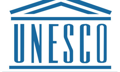 UNESCO logo in blue with a stylized roof motif above and lines framing the word UNESCO