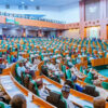 Large legislative chamber filled with lawmakers seated in green and orange seats, with a podium on the right and spectators along the balconies above.