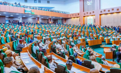 Large legislative chamber filled with lawmakers seated in green and orange seats, with a podium on the right and spectators along the balconies above.