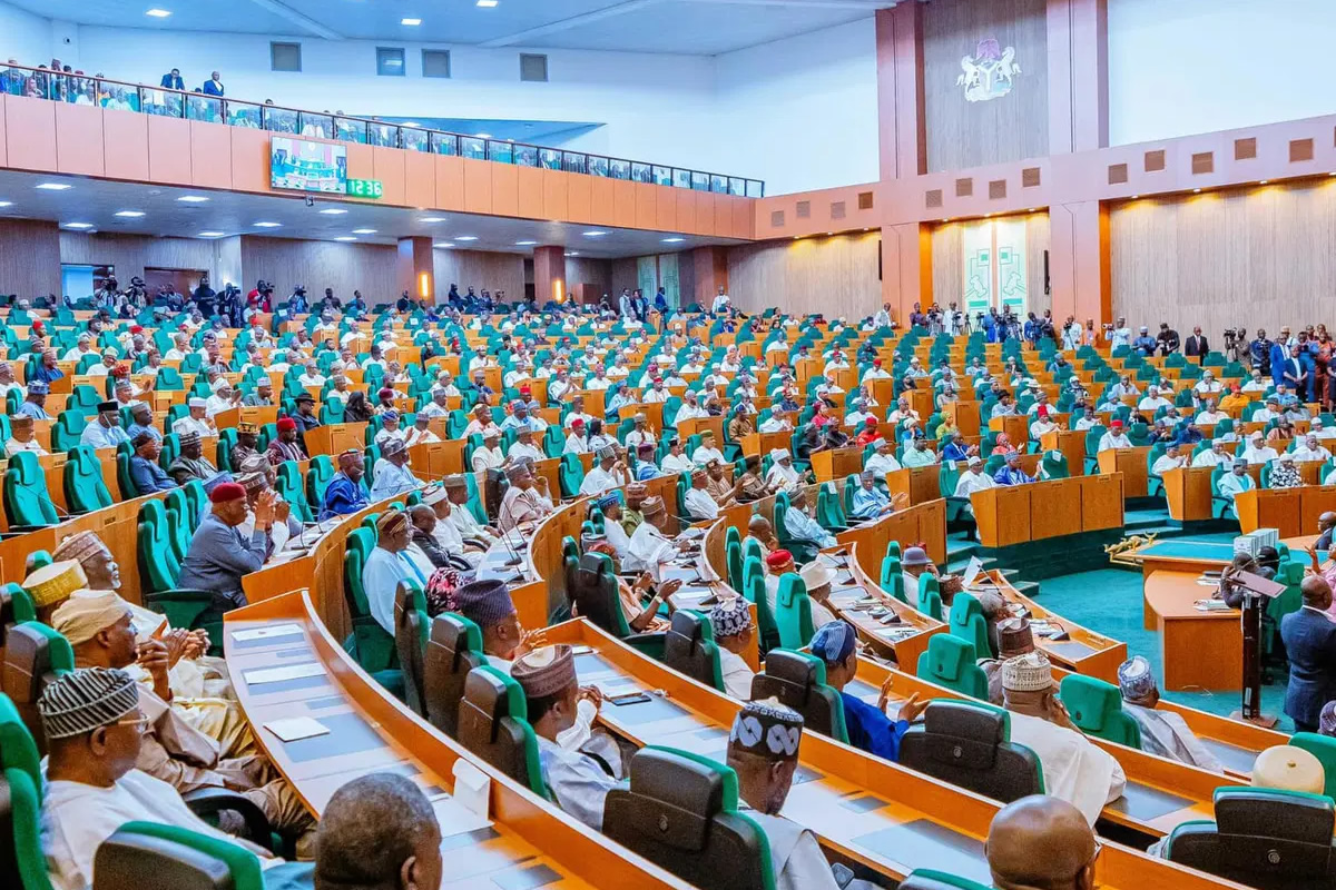 Large legislative chamber filled with lawmakers seated in green and orange seats, with a podium on the right and spectators along the balconies above.
