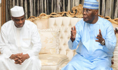 Two men in traditional robes sit on a tufted cream sofa, engaged in a thoughtful discussion with hand gestures.