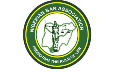 Circular logo of the Nigerian Bar Association with the slogan 'Promoting the Rule of Law' around the rim and a central figure holding scales over a map outline of Nigeria, in green and yellow.