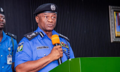 Police officer in blue uniform speaks at a green podium, holding an orange microphone.