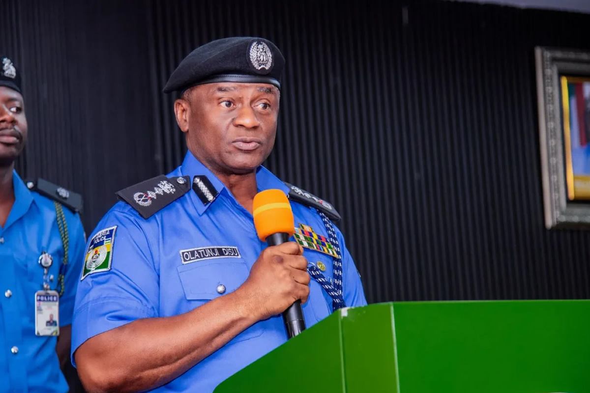 Police officer in blue uniform speaks at a green podium, holding an orange microphone.