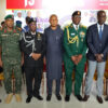 Eight men in military uniforms and a civilian pose for a group photo indoors.