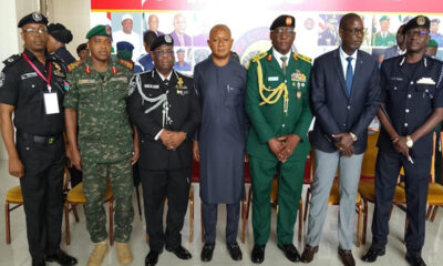 Eight men in military uniforms and a civilian pose for a group photo indoors.