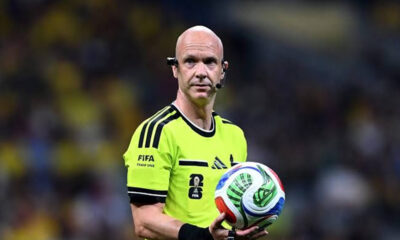Male soccer referee in a neon yellow kit holding a colorful FIFA match ball during a game.