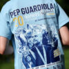Back view of a person wearing a light-blue T-shirt celebrating Pep Guardiola's 20 trophies with trophy images on the shirt logo.