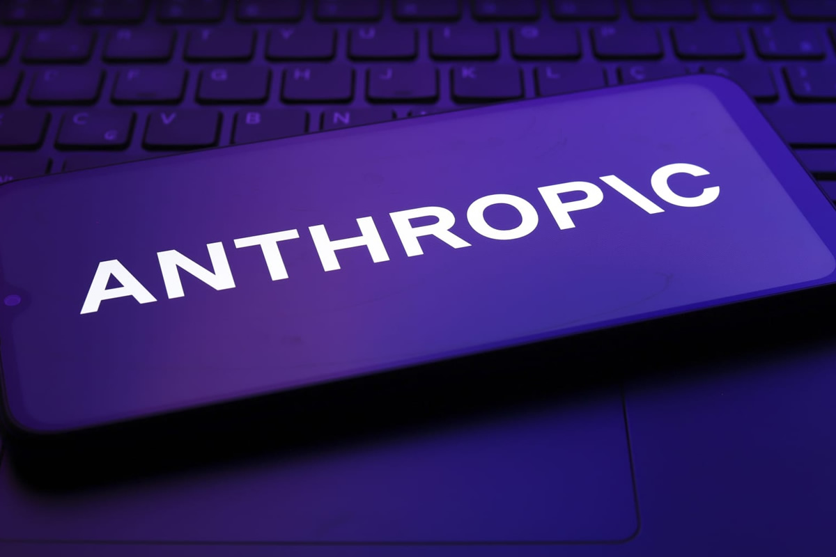 Smartphone screen showing the word ANTHROPIC in bold white letters, illuminated by a purple glow over a keyboard backdrop.
