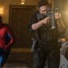 Spider-Man runs beside a armed soldier firing a rifle in a dimly lit hallway.