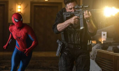 Spider-Man runs beside a armed soldier firing a rifle in a dimly lit hallway.