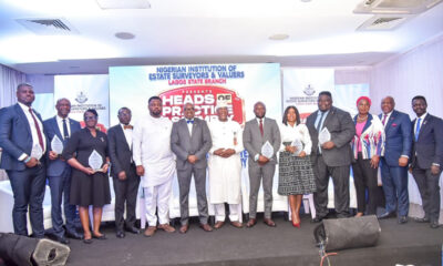 Group of professionals in suits and dresses posing with glass awards on a stage during an awards ceremony.