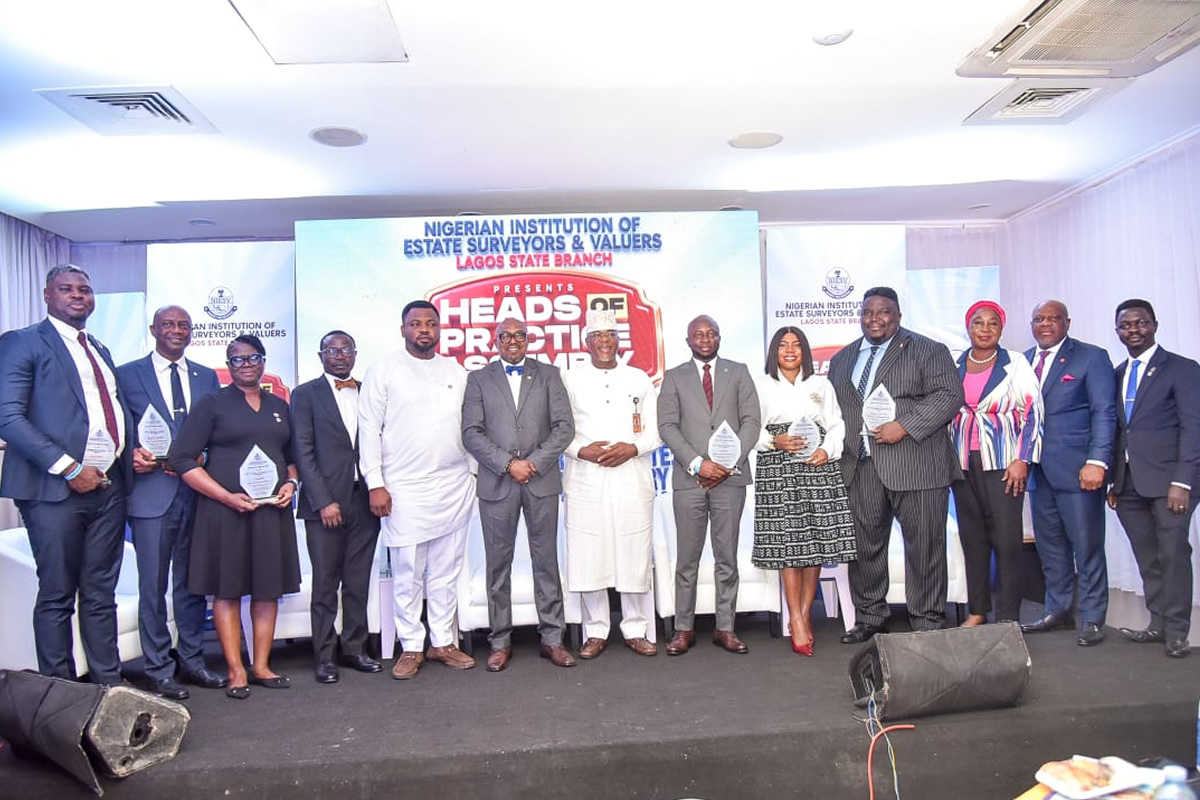 Group of professionals in suits and dresses posing with glass awards on a stage during an awards ceremony.