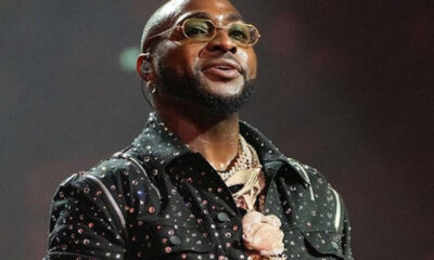Hip-hop artist on stage wearing a studded black shirt, gold chains, and glasses, looking upward while performing.