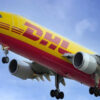 DHL cargo plane with yellow and red livery, landing with gear down against a blue sky.