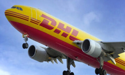 DHL cargo plane with yellow and red livery, landing with gear down against a blue sky.