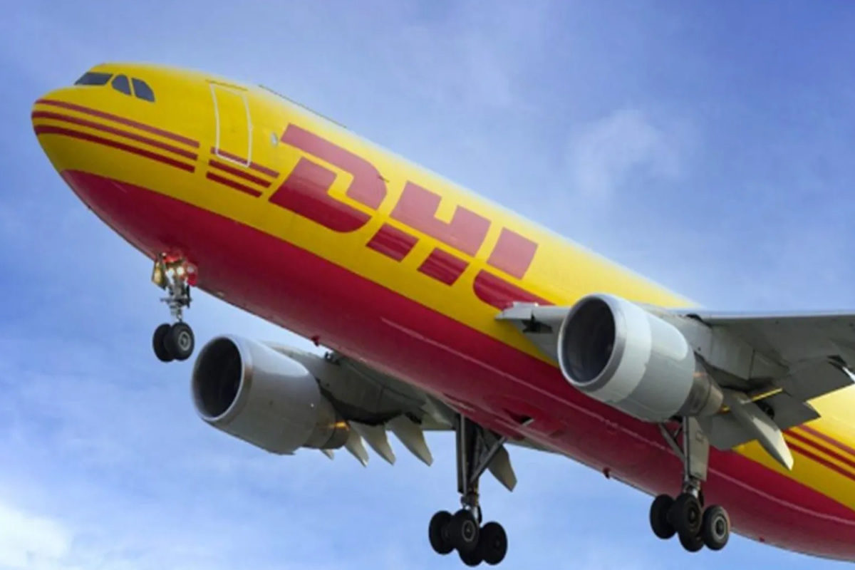 DHL cargo plane with yellow and red livery, landing with gear down against a blue sky.