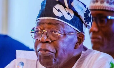 Elderly man with round glasses and a blue patterned traditional cap speaking at a meeting.