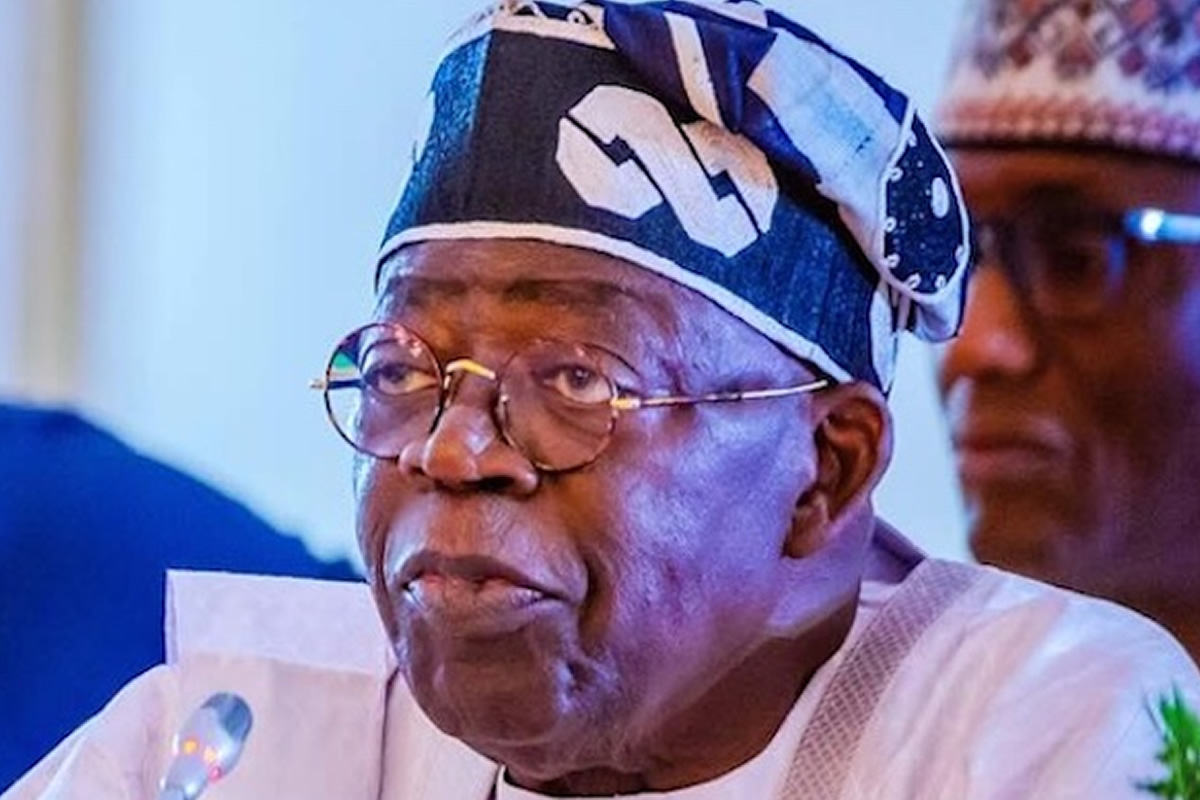 Elderly man with round glasses and a blue patterned traditional cap speaking at a meeting.