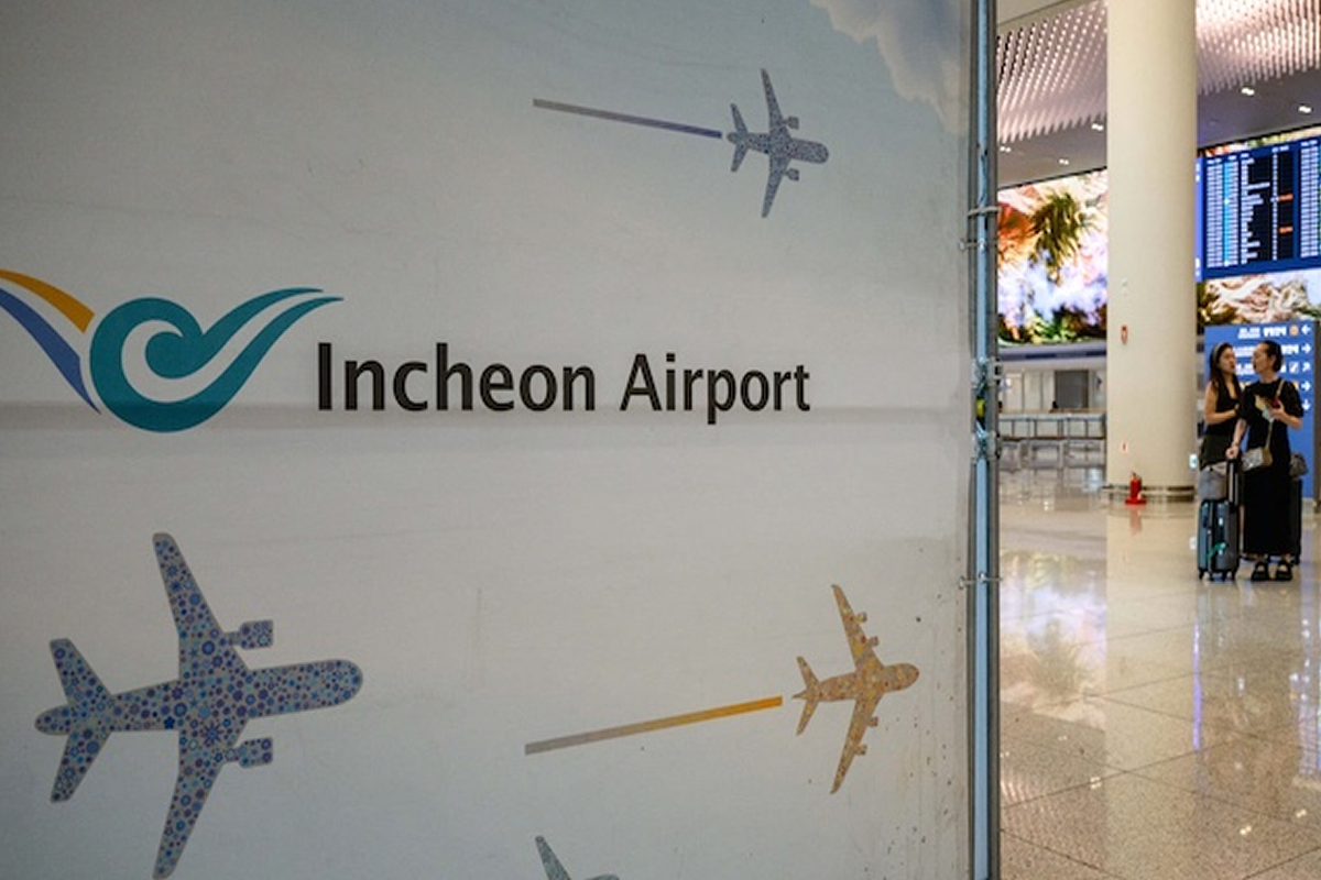 Wall graphic saying "Incheon Airport" with abstract airplane motifs; travelers with luggage visible in the background of a bright terminal