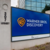 Outdoor sign at 307 Legget reading 'Warner Bros. Discovery' with WB shield logo on a blue panel at a corporate entrance site.
