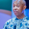 Man in a blue patterned dashiki speaks into a handheld microphone at an event.