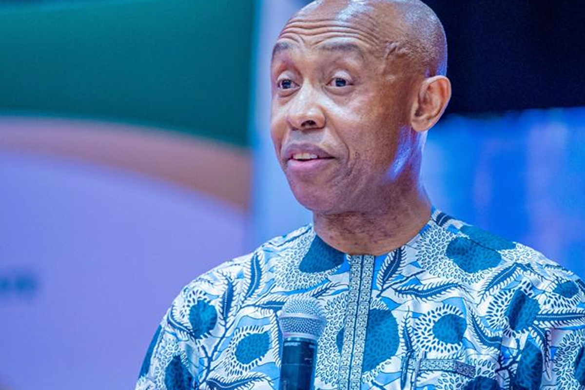 Man in a blue patterned dashiki speaks into a handheld microphone at an event.